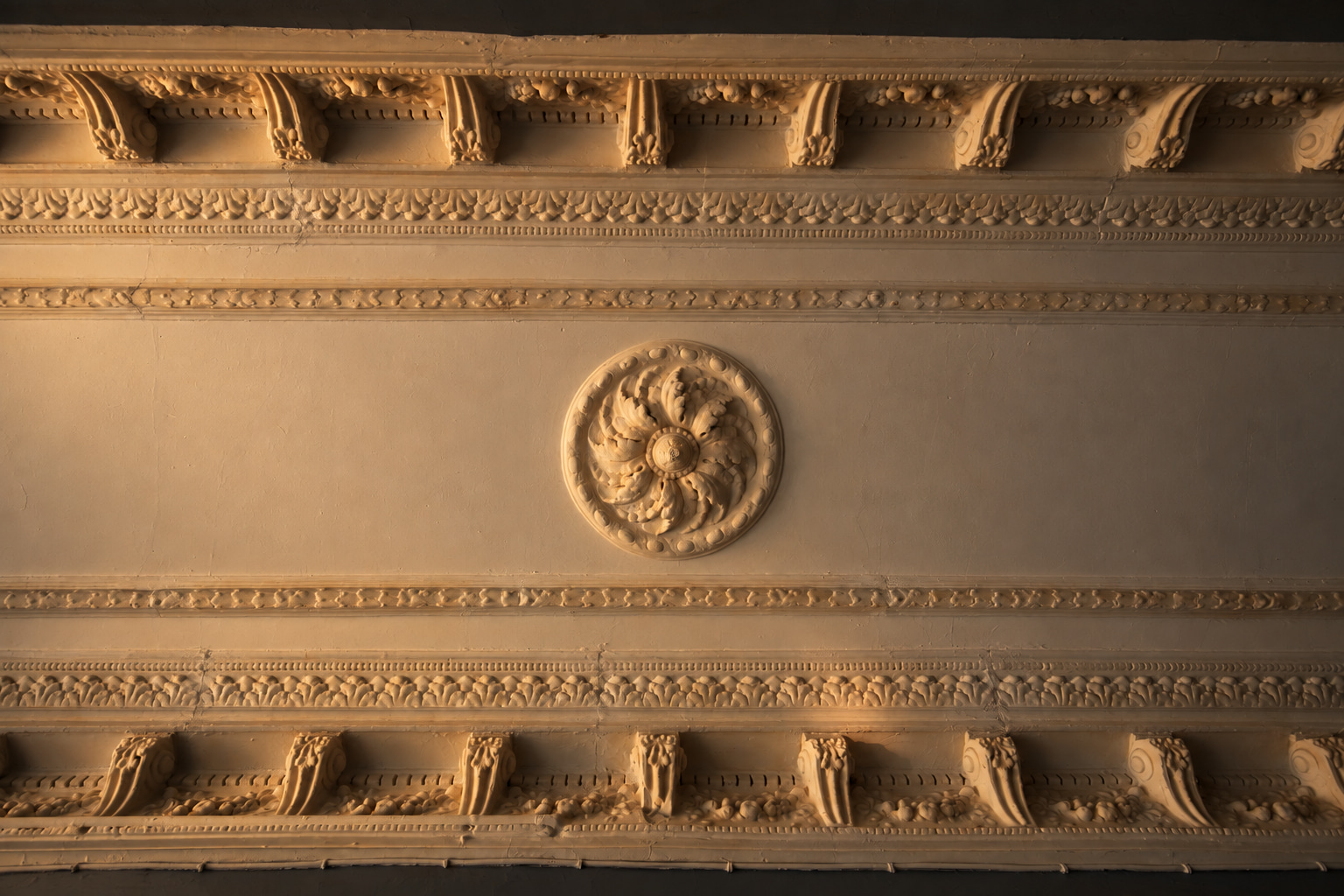Historic ornate plaster ceiling with a central rose and decorative cornices in warm light