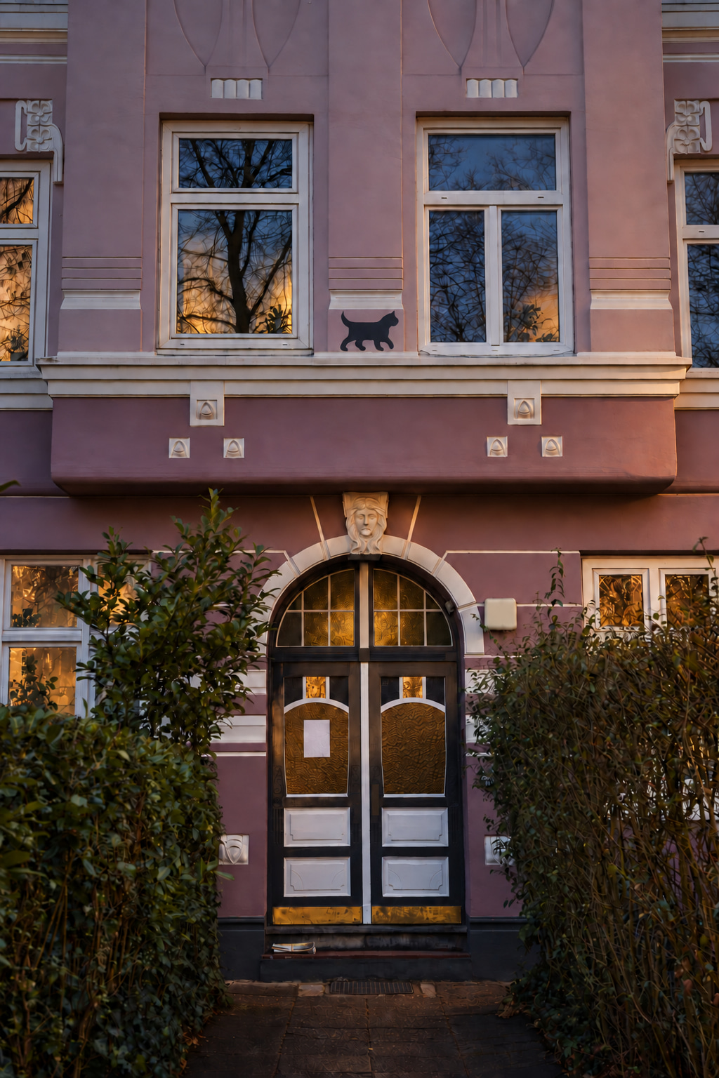 Pink period façade with a cat motif and historic entrance at dusk