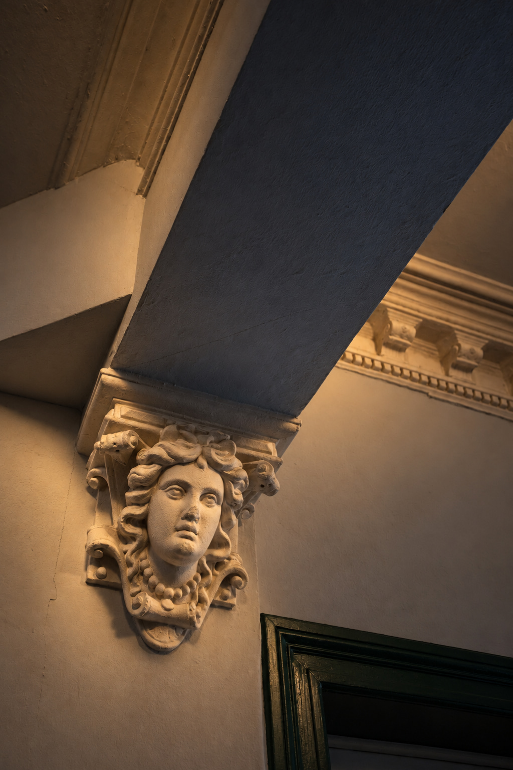 Figurative plaster corbel beneath a slate-blue arch in warm grazing light